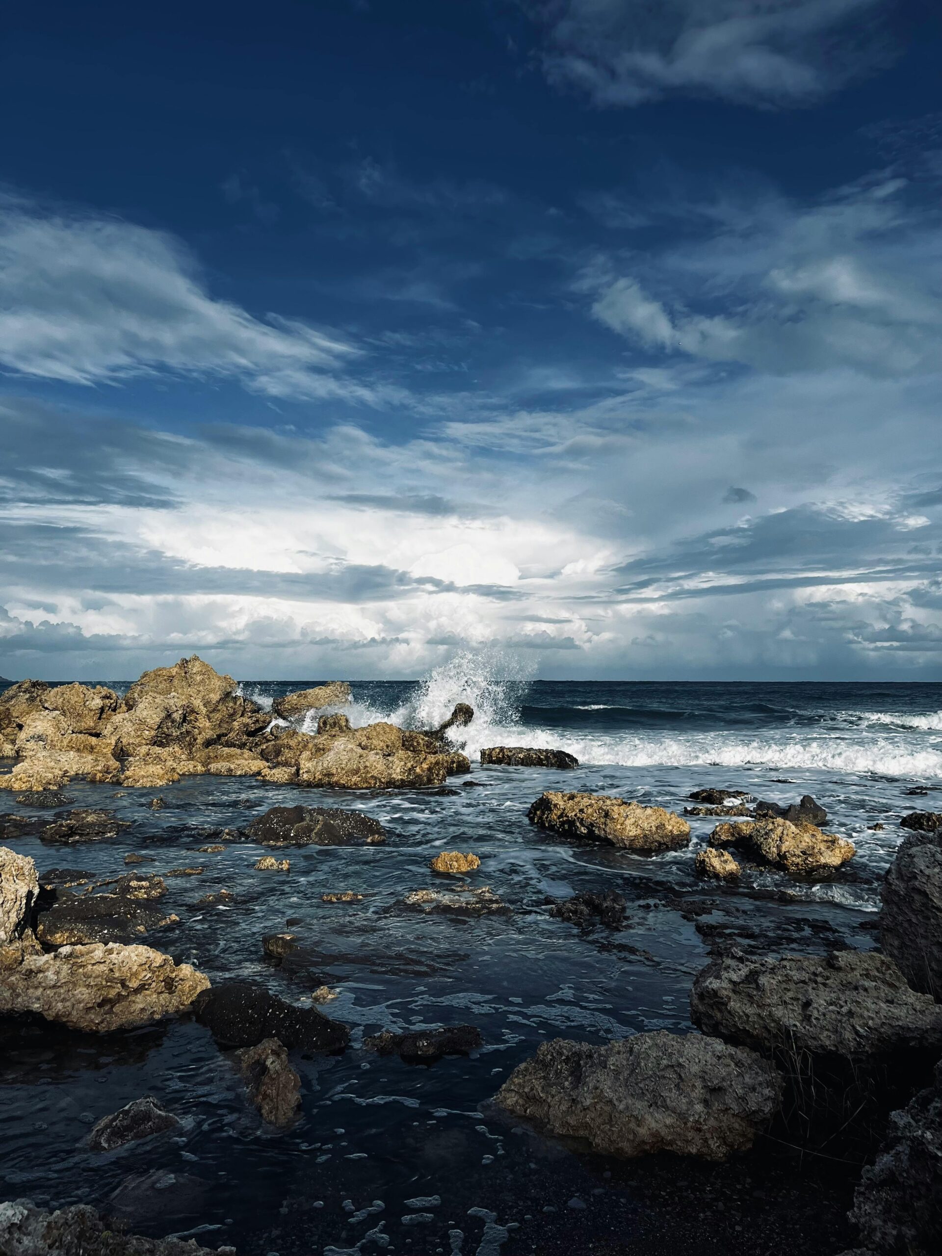 Dramatic ocean waves crashing on rocky shore under a dynamic sky.